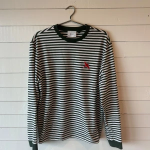 Axel Arigato Grönvit Randig Långärmad T-shirt, Storlek L - Väldigt bra skick, inga defekter förutom minimal fläck på lappen inne i tröjan. Tröjan är liten i storleken, jag skulle säga att den är som en medium. Nytvättad och från ett djur- och rökfritt hem.  Nypris: 900kr. Jag är 189 cm och väger 75 kg.