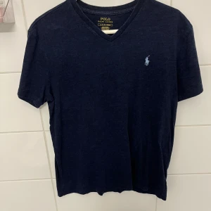Marinblå t-shirt från Polo Ralph Lauren - Säljer en stilren marinblå t-shirt från Polo Ralph Lauren. Den är V-ringad vid halsen. Frågor och funderingar? Hör bara av dig