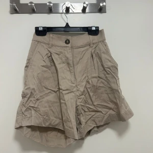 Kostymshorts - Beigebruna Kostymshorts. Snygga shorts som är lite högmidjade, i ett ”glansigt” material. De är superfina men lite små på mig.