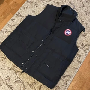 Canada Goose väst i svart, storlek L/G – Perfekt för vintern! - Säljer en svart Canada Goose väst i storlek L/G. Den är i bra skick, använd men välvårdad. Perfekt för kalla dagar med djupa fickor och dragkedja med knapplås. Rök- och djurfri.