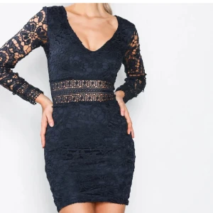 Mörkblå spetsklänning med lång ärm - Säljer en superfin mörkblå spetsklänning med v-ringning och långa ärmar. Klänningen har en tight passform och vackra spetsdetaljer. Perfekt för festliga tillfällen! Den har en dragkedja i ryggen 