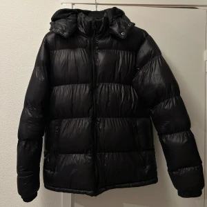 Svart pufferjacka - Säljer en svart pufferjacka som är perfekt för kalla dagar. Den har en dragkedja framtill och en mysig huva. Jackan är i bra skick och passar både till vardags och lite mer uppklädda tillfällen. Superbekväm och håller dig varm hela vintern!🩷