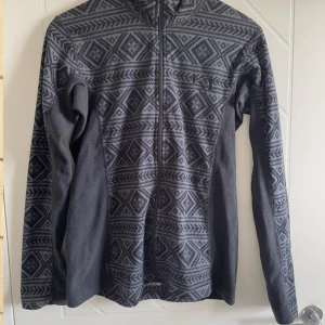 Fleece från Kari Traa - Mönstrad grå fleecejacka från Kari Traa i använt skick. Den är ganska tunn men perfekt som ett extralager. Aningen liten i storleken