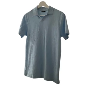 Ljusblå pikétröja - Säljer en stilren ljusblå pikétröja i bomull. Perfekt för sommardagar eller en avslappnad vårlook. Tröjan har korta ärmar och en klassisk krage. Passar både till vardags och lite finare tillfällen.