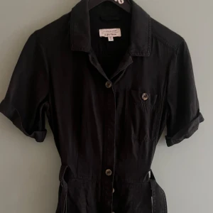 Svart byxdress / jumpsuit - Svart byxdress med bruna knappar från & Other Stories. Använd men fint skick utan anmärkningar.   Originalpris 900. 