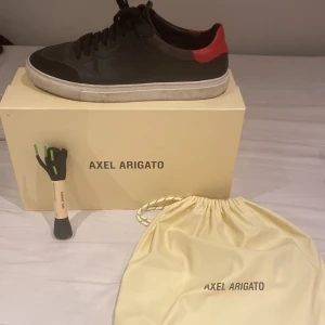 Feta Axel Arigato skor med en svart grund och lite rött - Tja, Jag säljer dessa sköna pjucks nu till nån lycklig person för endast 1800 när ny pris var 2750kr då jag nu inte längre kan ha dem längre tyvärr då dem är för små har använt sparsamt men haft en hel del därför priset så lågt. Skriv gärna vid frågo