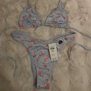 Blommig bikini från Hollister - Superfin bikini från Hollister i ljusblått med blommigt mönster. Den har knytband både i ryggen och nacken. Den är oanvänd och lapp finns kvar på underdelen. Trosan är i s och toppen i xs🥰inköpspris ca 500kr