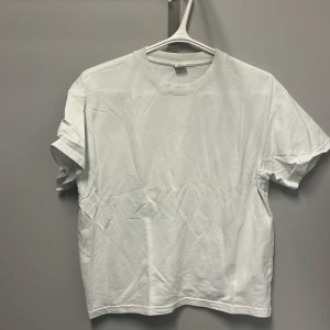 Vit t-shirt från Lindex - Säljer en klassisk vit t-shirt från Lindex i storlek 158/164. Perfekt för vardagsbruk med sin enkla och stilrena design. T-shirten är kortärmad och gjord i mjukt bomullsmaterial, vilket gör den bekväm att bära hela dagen. Passar perfekt till både jeans och shorts!