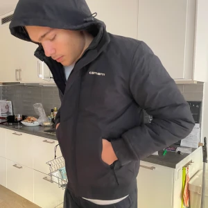 Svart jacka från Carhartt - Säljer en svart Carhartt jacka i storlek M. Den är perfekt för höst och vinter med sitt varma foder. Jackan har en dragkedja och är långärmad med en skön passform. Den är i mycket bra skick o fett snygg och ganska kort