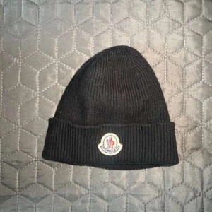 Moncler Mössa - Svart Moncler-mössa i toppskick, äkta vara (saknar kvitto). Nypris 1800 kr, säljes för endast 450 kr. Exklusiv och stilren, perfekt för kyliga dagar. 🤩💫 PS. Pris kan diskuteras!