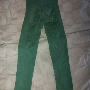 Gröna träningstigths med butt scrunch - Säljer ett par gröna leggings i storlek M. De är tillverkade av 90% polyamid och 10% elastan, vilket gör dem superstretchiga och bekväma. Perfekta för träning eller en avslappnad dag hemma. De har en tight passform och är i mycket bra skick.