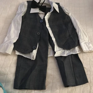 Barnens formella klädsel - Märke Name It - Passar för 1,5 till 2 år - Denna outfit inkluderar en vit skjorta med klassisk krage, en väst och mörka rutiga byxor, vilket ger barnet ett stilrent och formellt utseende nästan nytt (en gång använt)