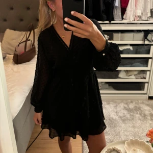 Svart klänning med prickar - Snygg svart klänning med diskreta prickar och v-ringad hals. Den har långa ärmar och en smickrande passform med resår i midjan. Perfekt för både fest och vardag! 🖤