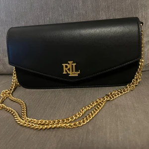 Ralp Lauren väska  - Säljer min Lauren Ralph Lauren NAPPA LEATHER MEDIUM SAWYER BAG - Across body bag - black Fin väska från Ralph Lauren i svart och guld. Du kan välja att ha den som Cross body eller på axeln.  Dustbag medföljer.  Nypris 3995:-  Säljer den för 1700:-  