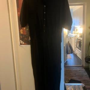 Svart klänning från Totême - Säljer en elegant svart klänning från Totême i storlek XS. Klänningen har korta ärmar och knappar framtill, vilket ger en stilren look. Materialet är en blandning av viskos och nylon, vilket gör den både bekväm och hållbar. Perfekt för både vardag och fest!