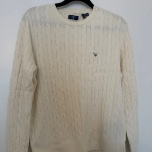 Vit stickad tröja från Gant strl 170/15år - Säljer en stilren vit stickad tröja från Gant för killar i strl 170/15år.  Den har ett klassiskt kabelstickat mönster och en liten broderad logga på bröstet. Perfekt för både höst och vinter, och den är supermysig att ha på sig. Passar till alla tillfällen!