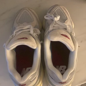 Vita sneakers från New Balance - Säljer ett par vita New Balance sneakers i mycket bra skick. De har en snygg design med röda detaljer och en bekväm sula. Perfekta för både vardag och träning. Skorna är i storlek herr 42 och har klassisk snörning.