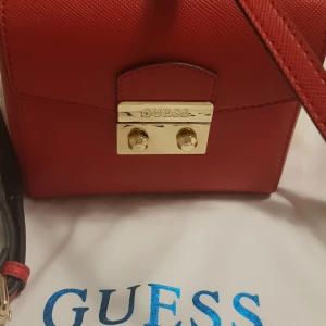 Väskor  - Jag säljer min fina väska Guess axelväska mycket bra skick använd 1gång inga skador ej smutsig, men stått i garderoben ett bra tag,,,,Hör av dig vid intresse,,,,,,,