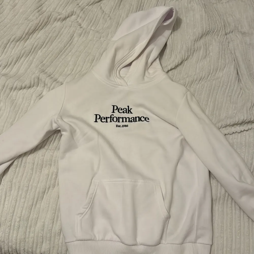 Säljer en stilren vit hoodie från Peak Performance. Den har en klassisk design med loggan broderad på framsidan. Perfekt för både vardag och träning. Hoodien har en stor ficka fram och är i mycket bra skick. Passar perfekt för höst och vår! 😍🤍. Tröjor & Koftor.