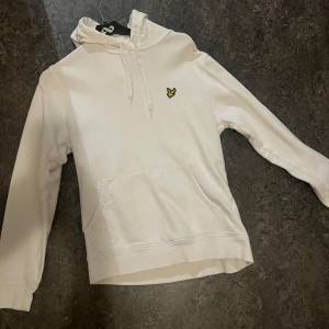 Vit hoodie från Lyle & Scott - Säljer en stilren vit hoodie från Lyle & Scott med deras ikoniska logga på bröstet. Den har en klassisk känguruficka och justerbar huva med snören. Perfekt för en avslappnad stil eller lager på lager under kallare dagar. 🕊️
