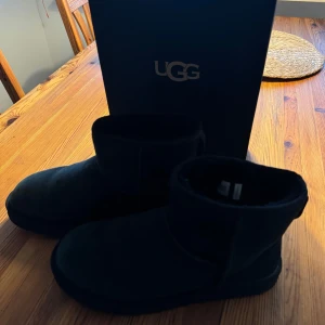 Svarta UGG boots - Säljer ett par svarta UGG boots i mocka. De är i mycket bra skick och perfekta för höst och vinter. Skorna har en robust sula och är superbekväma. Perfekta för att hålla fötterna varma och stiliga under kalla dagar.