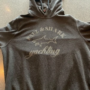 Grå hoodie från Paul & Shark - Säljer en snygg grå hoodie från Paul & Shark med deras ikoniska hajlogga och texten 'yachting' på framsidan. Den är i superfint skick och perfekt för hösten och vintern! Nypris ca 2000 men säjer ändast för 700kr, priser går att diskuteras. hör av vid fler frågor!🙌