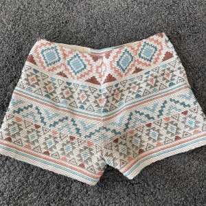 Mönstrade shorts med dragkedja - Säljer ett par unika shorts med ett färgglatt mönster i blått, rött och beige. De har en dragkedja bak och är perfekta för sommardagar. Passar både till vardags och festliga tillfällen!