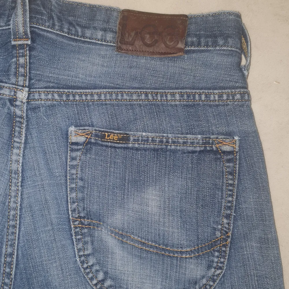 Säljer ett par klassiska blå jeans från Lee i bra skick. De har en snygg slitning på framsidan och är tillverkade i slitstarkt denim. Perfekta för vardagsbruk med en straight passform som ger en tidlös look. Passar både till sneakers och kängor!. Jeans & Byxor.