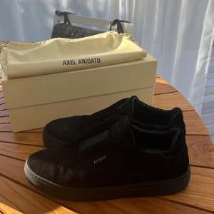 Axel Arigatos 360 Laceless - Säljer ett par stilrena svarta sneakers från Axel Arigato i mycket bra skick. Skorna är gjorda i mocka och har en minimalistisk design utan snörning. Perfekta för både vardag och fest! Kommer med originalförpackning och dustbag.