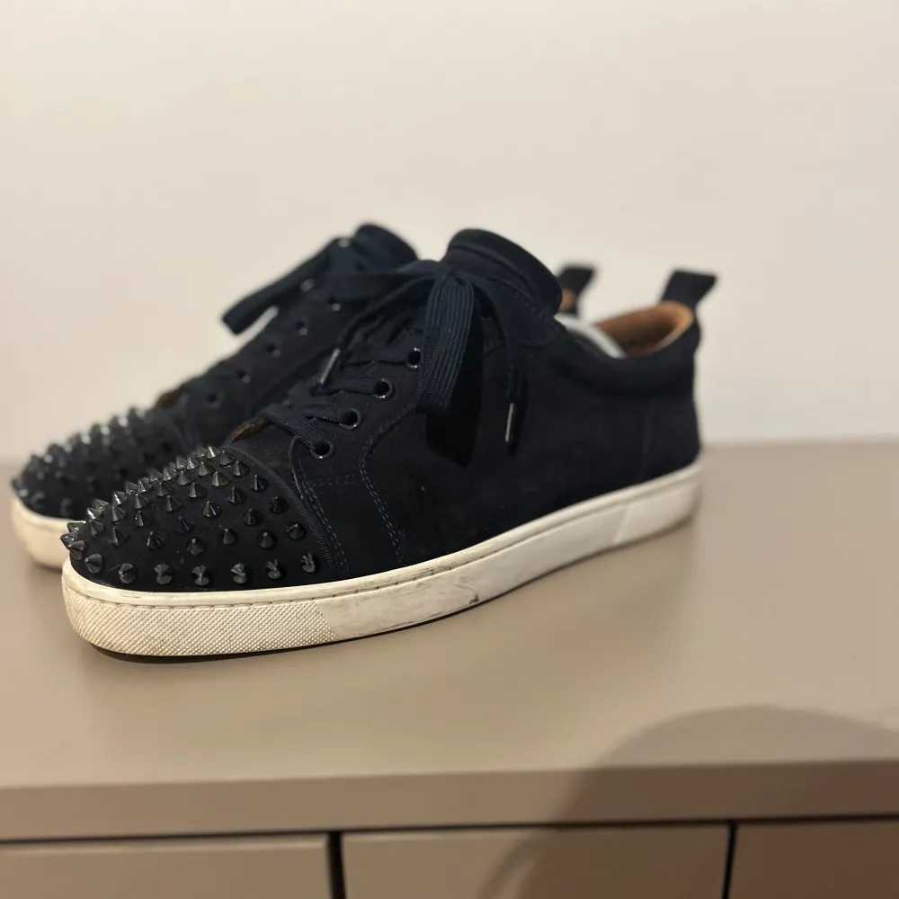 Säljer ett par marinblå sneakers från Christian Louboutin. Skorna är i väldigt fint skick men har en liten defekt på insidan som inte syns när dom sitter på. Skorna är i storlek 44 men sitter en aning större. Box, dustbags och kvitto medföljer. Skorna är lite smutsiga för tillfället men om du vill tvättar vi skorna innan frakt. Kan gå ner i pris vid snabb affär. Hör av dig vid frågor!. Skor.