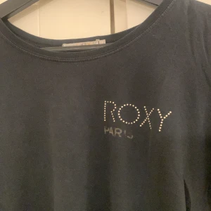 Marinblå t-shirt från Roxy - Snygg marinblå  t-shirt från Roxy med glittrande detaljer på framsidan. Den har korta ärmar och ett snyggt tryck på baksidan. Är i storlek L men skulle igentligen säga S/M då den passar mig som brukar ha S.