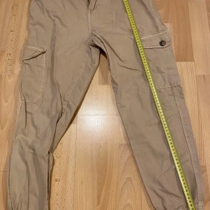 Beige cargobyxor från Lager 157 - Säljer ett par beige cargobyxor från Lager 157. Byxorna har flera praktiska fickor och är tillverkade i 100% bomull. Perfekta för en avslappnad stil med en bekväm passform.❤️ Saknar en knapp på baksidan och finns en röd läppstift märke vid knät.