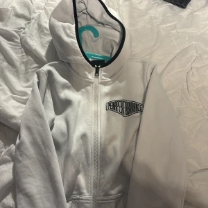 Vit huvtröja med dragkedja - Säljer en vit huvtröja med dragkedja från Performance. Tröjan har en stilren design med svart kant på huvan och ett tryck på bröstet. Perfekt för en avslappnad stil.