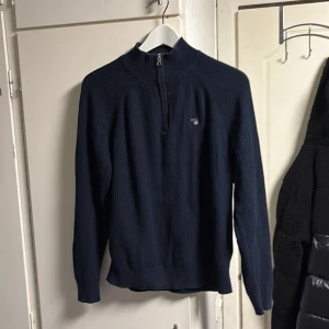 Mörkblå stickad tröja från Gant - Säljer en stilren mörkblå stickad tröja från Gant med dragkedja vid halsen. Tröjan har långa ärmar och ett diskret broderat märke på bröstet. Perfekt för kyligare dagar. PRIS KAN DISKUTERAS!