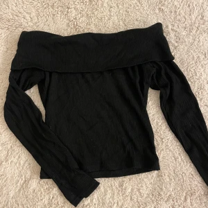Svart ribbad offshoulder topp från Gina Tricot - Snygg svart ribbad offshoulder topp från Gina Tricot. Perfekt för en stilren look med långa ärmar och en bekväm passform. Passar utmärkt till både jeans och kjol. Hör av er vid frågor💗