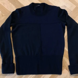 Svart ulltröja från COS - Säljer en stilren svart tröja från COS. Tröjan har långa ärmar och en ribbad kant vid ärmslut och nederkant. Perfekt för en minimalistisk look.