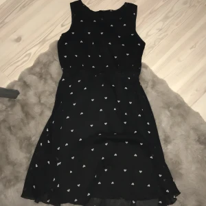 Svart klänning med hjärtan från KappAhl - Charmig svart klänning från KappAhl med små vita hjärtan. Klänningen har en spetsdetalj vid nacken där bak och är ärmlös. 