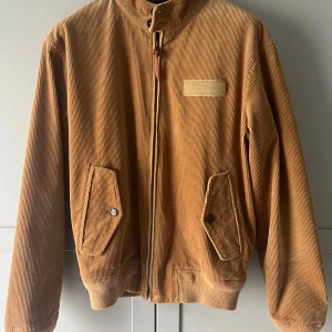 Brun manchesterjacka från Polo Ralph Lauren - Säljer en snygg brun manchesterjacka från Polo Ralph Lauren. Jackan har en dragkedja framtill och två fickor med knappar. Perfekt för höst och vår med sin stilrena design och bekväma passform.