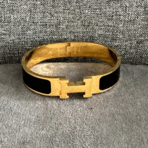 Guld och svart armband - Elegant armband i guld pläterat rostfritt stål med svart emaljdetalj stilrent. Perfekt för att ge en lyxig touch till din outfit.