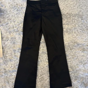 Svarta kostymbyxor - Snygga svarta kostymbyxor med bootcut-stil. Perfekta för en stilren look. Byxorna har en medelhögmidja och stängs med knappar. Lappen är tyvärr borta. Skulle gissa på storlek 34!