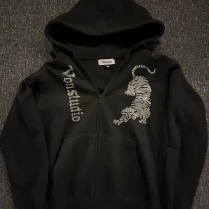 Svart hoodie från Vonstudio - Säljer en svart hoodie från Vonstudio med dragkedja och coolt tryck av en tiger på framsidan. Bra skick, lite nopprig men annars väldigt bra. Säljer för jag växt ur den.
