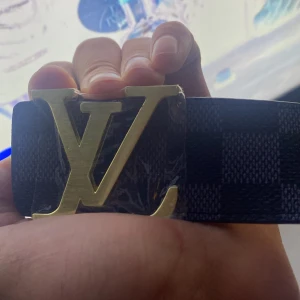 bälte - det är ett läder bälte med svart o grå mömster rutigt.