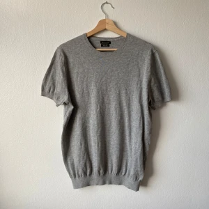Grå Massimo Dutti kortärmad tröja - Säljer en stilren grå kortärmad tröja från Massimo Dutti i extra fin bomull. Perfekt för en avslappnad och bekväm stil. Tröjan har en klassisk rund hals och ribbade kanter.