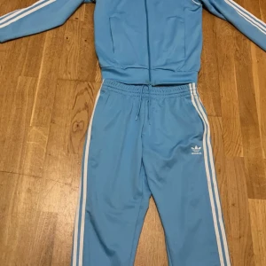 Ljus Blå Adidas SST tracksuit - ljus blå adidas kofta i storlek S och adidas byxor i storlek M. Perfekt till vår och sommar