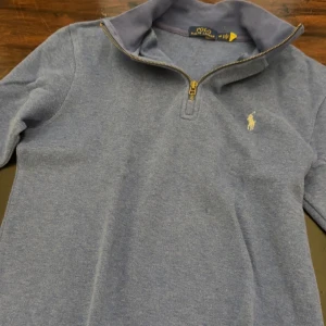 Blå tröja med dragkedja från Polo Ralph Lauren - Säljer en stilren blå tröja från Polo Ralph Lauren med halv dragkedja och klassisk logga på bröstet. Perfekt för en avslappnad men snygg look. Tröjan har långa ärmar och en bekväm passform. Pris kan diskuteras!