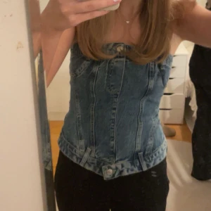 Jeanskorsett i blå denim - Trendig jeanskorsett i blå denim med dragkedja bak och knappdetaljer fram. Perfekt för en stilren look. Endast använd en gång.