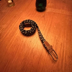 Flätat bälte  - Snyggt flätat bälte i svart, mörkblått och vitt. Perfekt för att ge en stilren touch till din outfit. Bältet har ett klassiskt metallspänne och är justerbart för bästa passform.