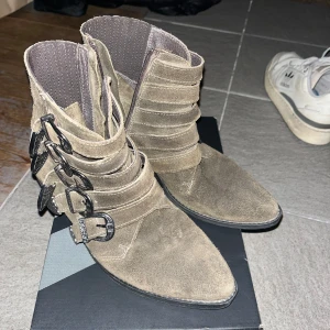 Bruna Pavement mocka boots med spännen - Snygga bruna boots i mocka med flera dekorativa spännen och spetsig tå. Perfekta för en stilren look med en touch av edge. Passar bra till både jeans och klänning.