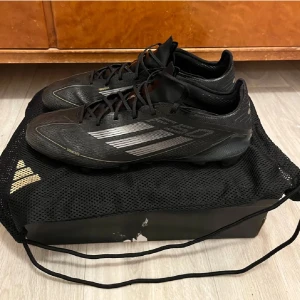 Svarta fotbollsskor från Adidas - Säljer ett par svarta fotbollsskor från Adidas med snörning och diskreta ränder i silver. Skorna har en strömlinjeformad design och är perfekta för snabba rörelser på planen.