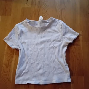 Vit ribbad topp - Säljer en stilren vit ribbad topp med korta ärmar. Perfekt för en avslappnad look.